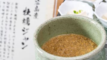 A ceramic bowl with a textured sauce, a menu with Japanese text, and small bowls with green garnishes.