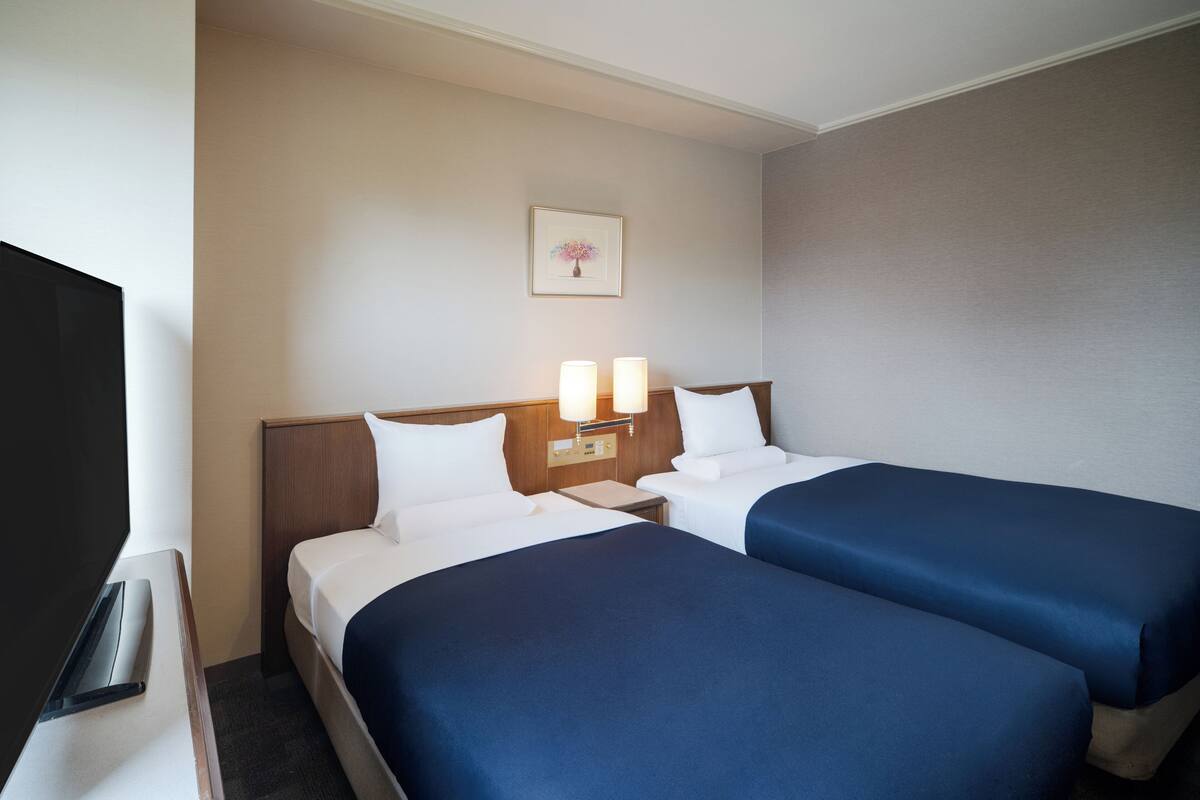 A hotel room with two beds, a TV, and a framed picture on the wall.