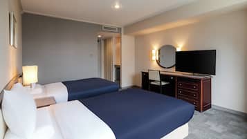 A hotel room with two beds, a desk with a chair, a television, and a mirror.