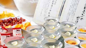 Una mesa con diversas opciones de comida y bebidas, incluyendo vasos con rodajas de limón, un bol de uvas y un plato con gajos de naranja.