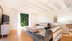 A cozy living room with a wooden floor, a sofa, a coffee table, and a TV on a stand. - Beachwood - Firepit - Pet Friendly - 2 Mins Walk to the Beach (Callala Beach)