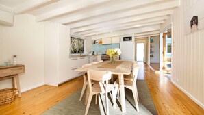 A spacious kitchen with white cabinets, a central island, and a dining area with a wooden table and chairs. - Beachwood - Firepit - Pet Friendly - 2 Mins Walk to the Beach (Callala Beach)