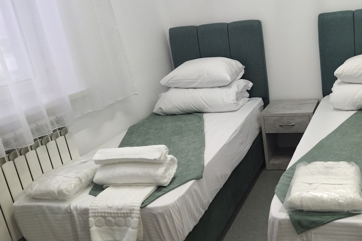 Two twin beds with green headboards, white bedding, and neatly folded towels.