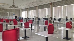 A spacious conference room with rows of tables and chairs, large windows with vertical blinds, and a chandelier. - Sulo Aksay Hotel (Aksay)