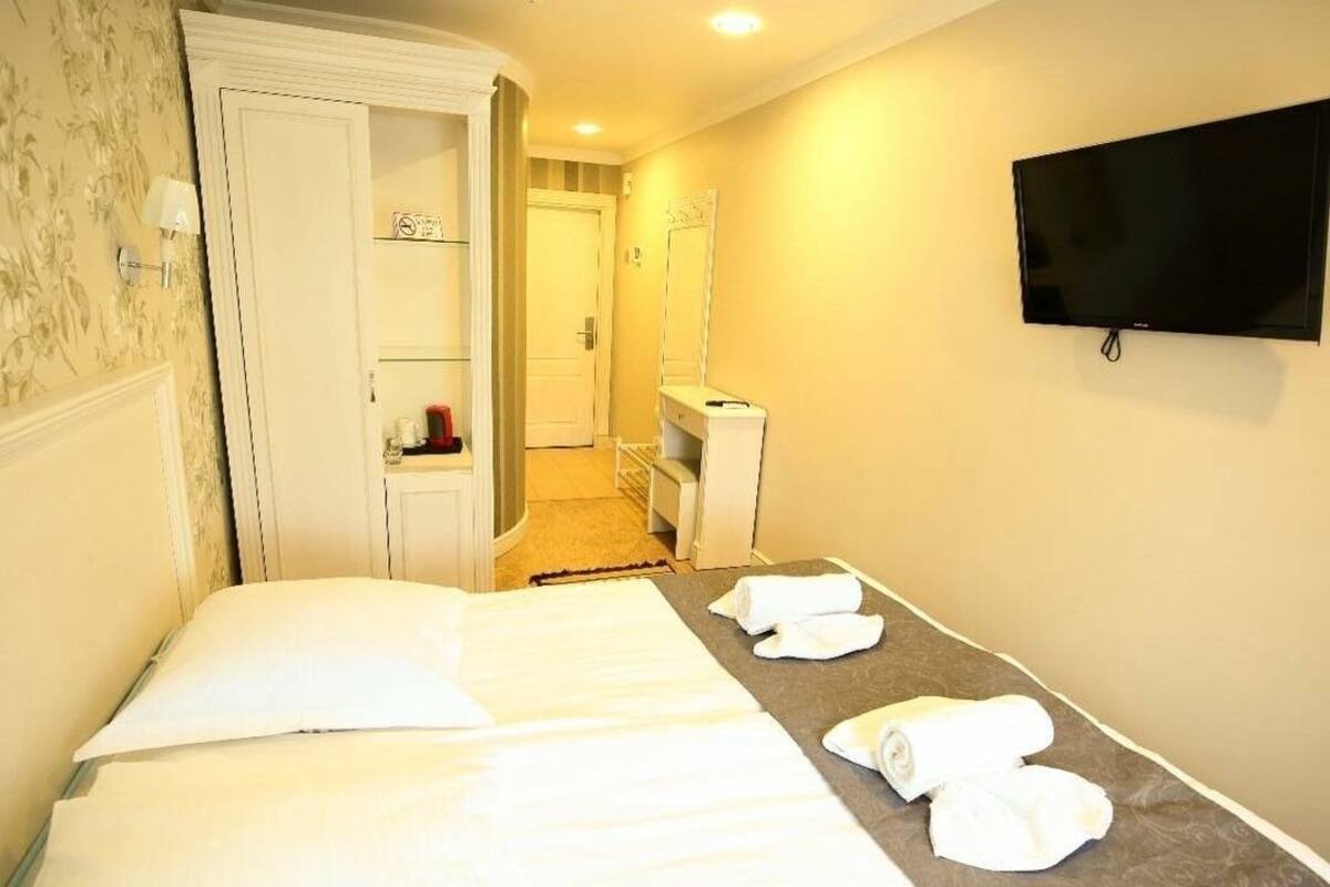 A hotel room with a bed, a TV mounted on the wall, and a bathroom visible through an open door.