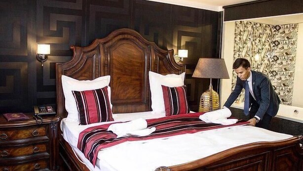 A neatly made bed with a wooden headboard, two bedside lamps, and a nightstand with a telephone. - Sulo Aksay Hotel (Aksay)