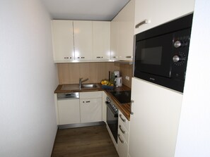 A compact kitchen with white cabinets, a stainless steel sink, a black oven, and a coffee maker on the countertop.