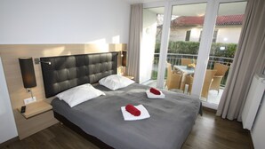 Quarto de hotel com uma cama grande, uma mesa de cabeceira, um abajur e vista para a varanda.
