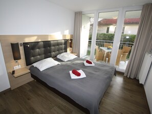 A hotel room with a large bed, a nightstand, a lamp, and a view of the outside balcony.