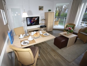 A modern dining area with a television, dining table set with plates, cups, and a basket of bread. - High Lith Apartment 3-05 (Cuxhaven)