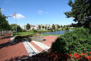 A paved walkway with a stone wall and flower beds, leading to a body of water with buildings in the background. - High Lith Apartment 3-05 (Cuxhaven)