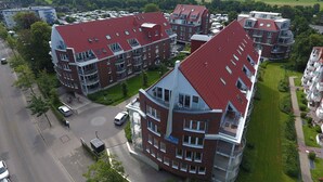 Um edifício residencial de vários andares com telhado vermelho, várias varandas e um gramado bem cuidado.