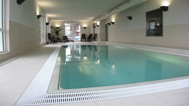 Piscina interna com água cristalina, cercada por paredes com luminárias embutidas.