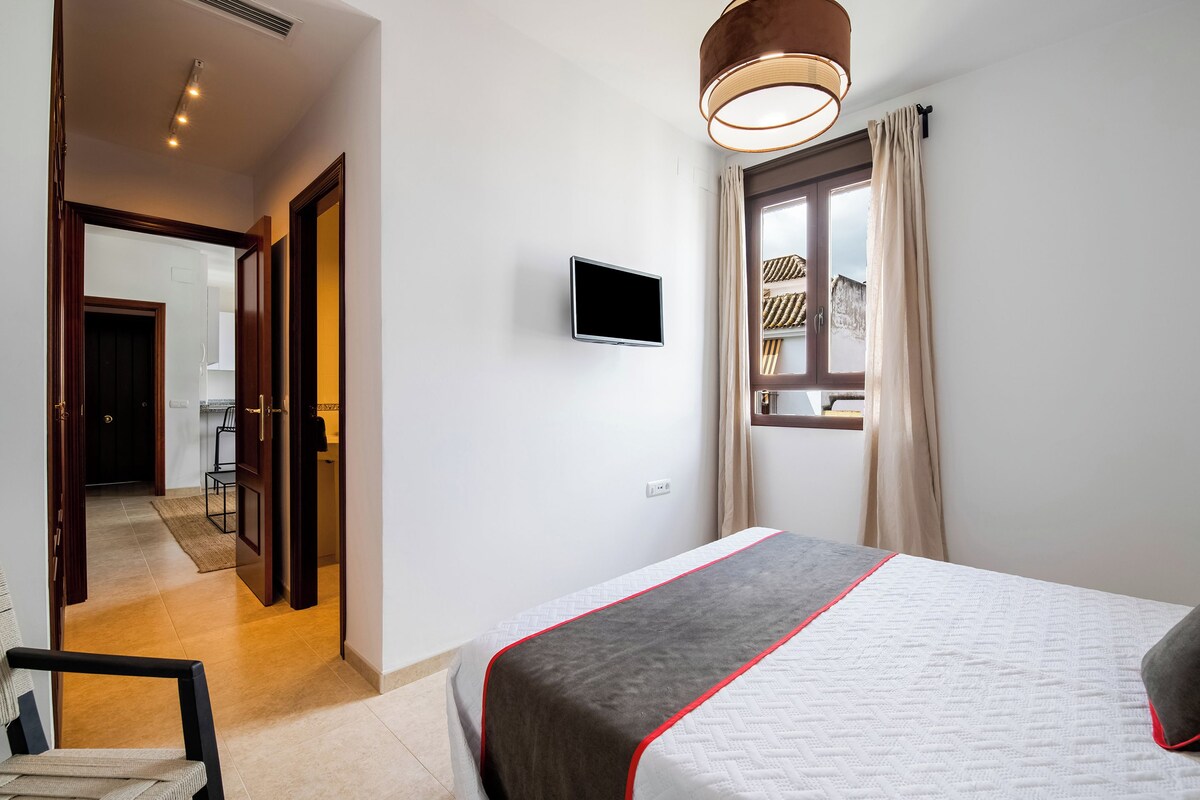 Una habitación de hotel con cama, televisión, ventana con cortinas y puerta que da a un baño.