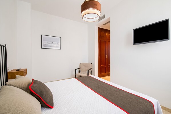 Una habitación de hotel con una cama, televisor, una silla y una puerta que da a otra habitación.