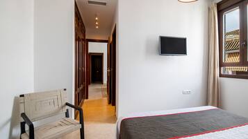 A hotel room with a bed, a television mounted on the wall, a chair, and a window with curtains.