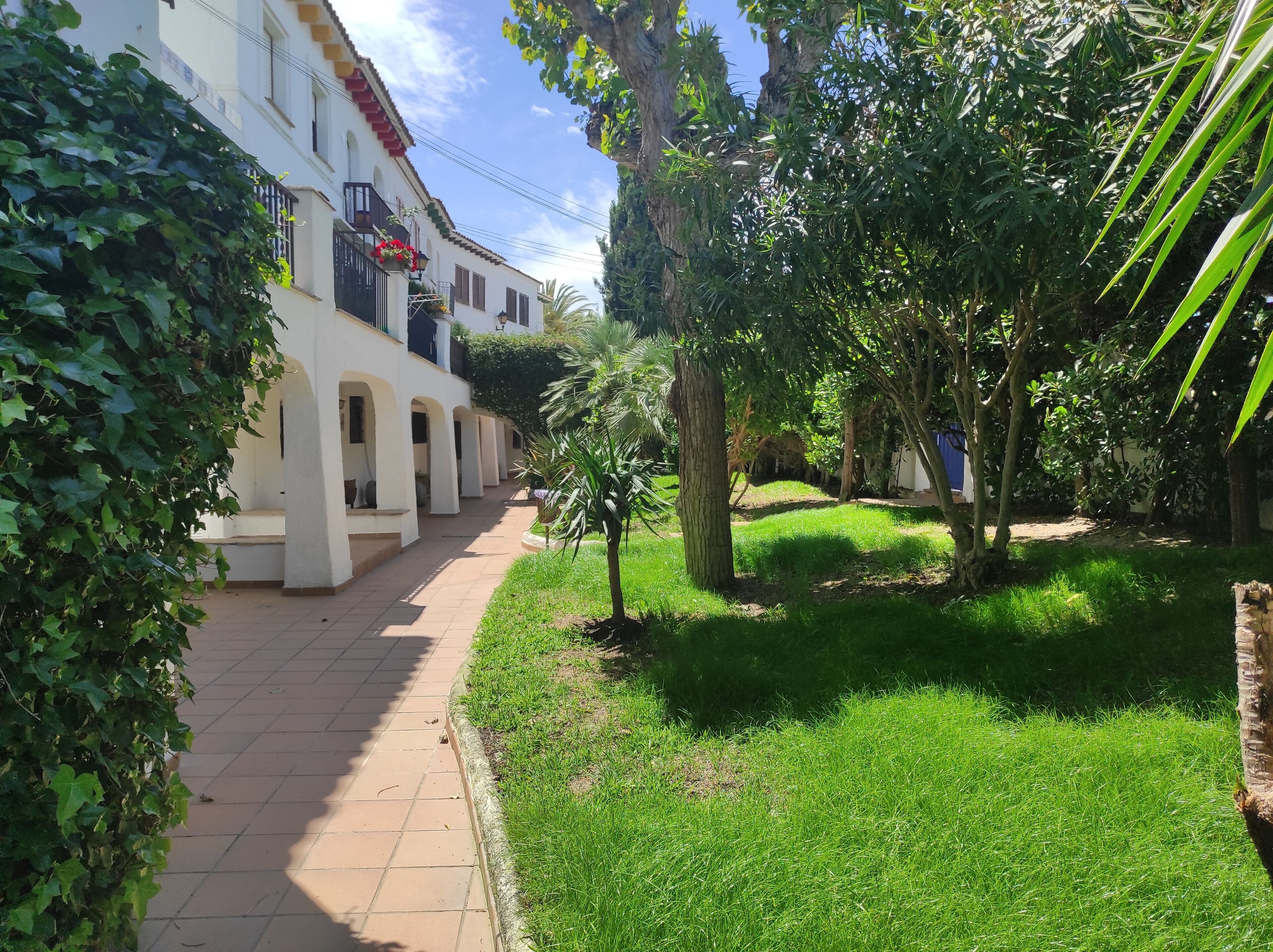Un sendero conduce a un edificio de paredes blancas y detalles rojos, rodeado de follaje y árboles.
