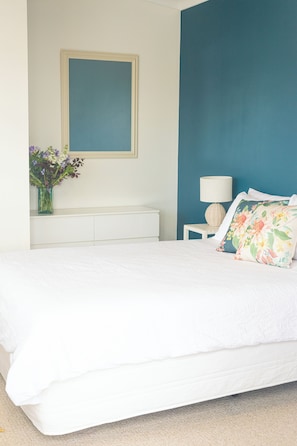 Une chambre à coucher comprenant un lit, une table de chevet, une lampe, un vase avec des fleurs et un cadre photo fixé au mur.