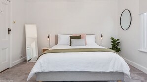 A bedroom with a bed, bedside lamps, a mirror, a potted plant, and a window.