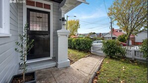 A residential house with a front porch, a black door, and a small tree in the front yard.