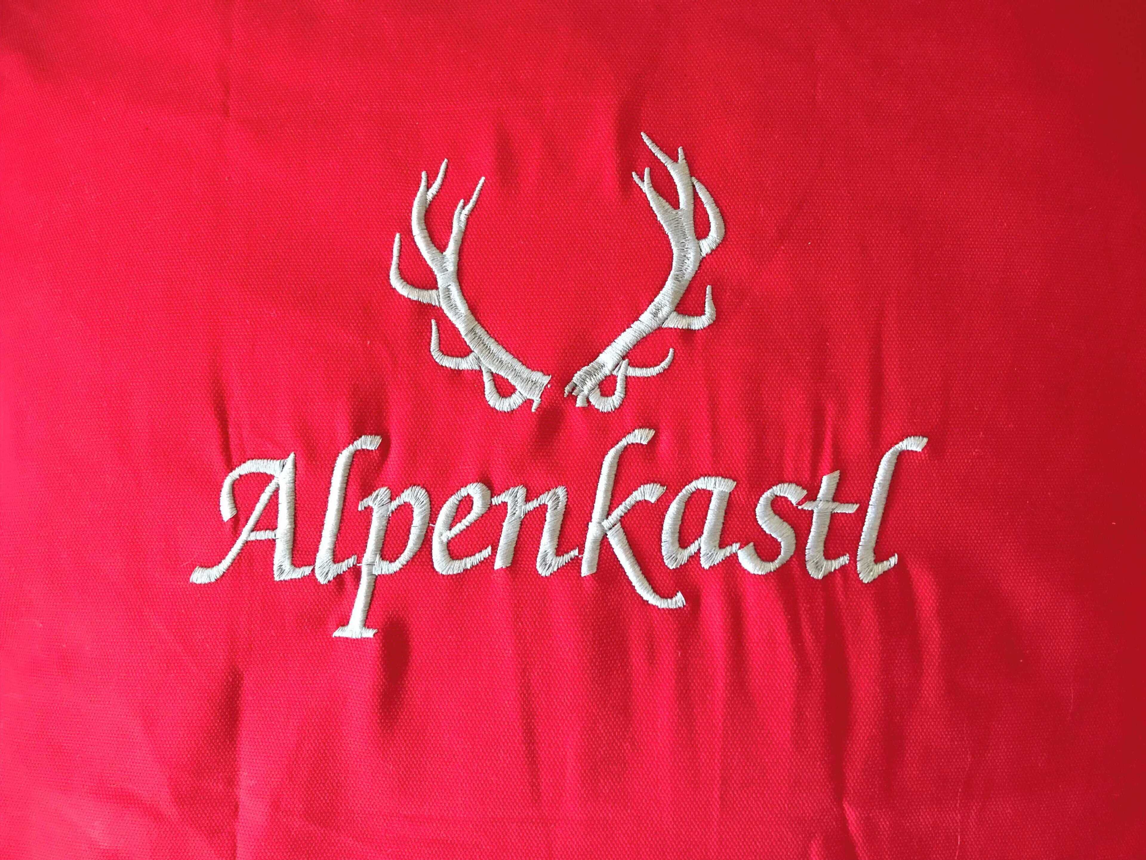 A red fabric with embroidered deer antlers and the text "Alpenkastl".