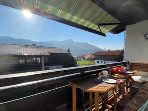 A balcony with a view of mountains, a dining table with plates and cups, and a striped awning.