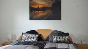 A bedroom with a bed, two bedside tables, and a painting of a sunset over a body of water.