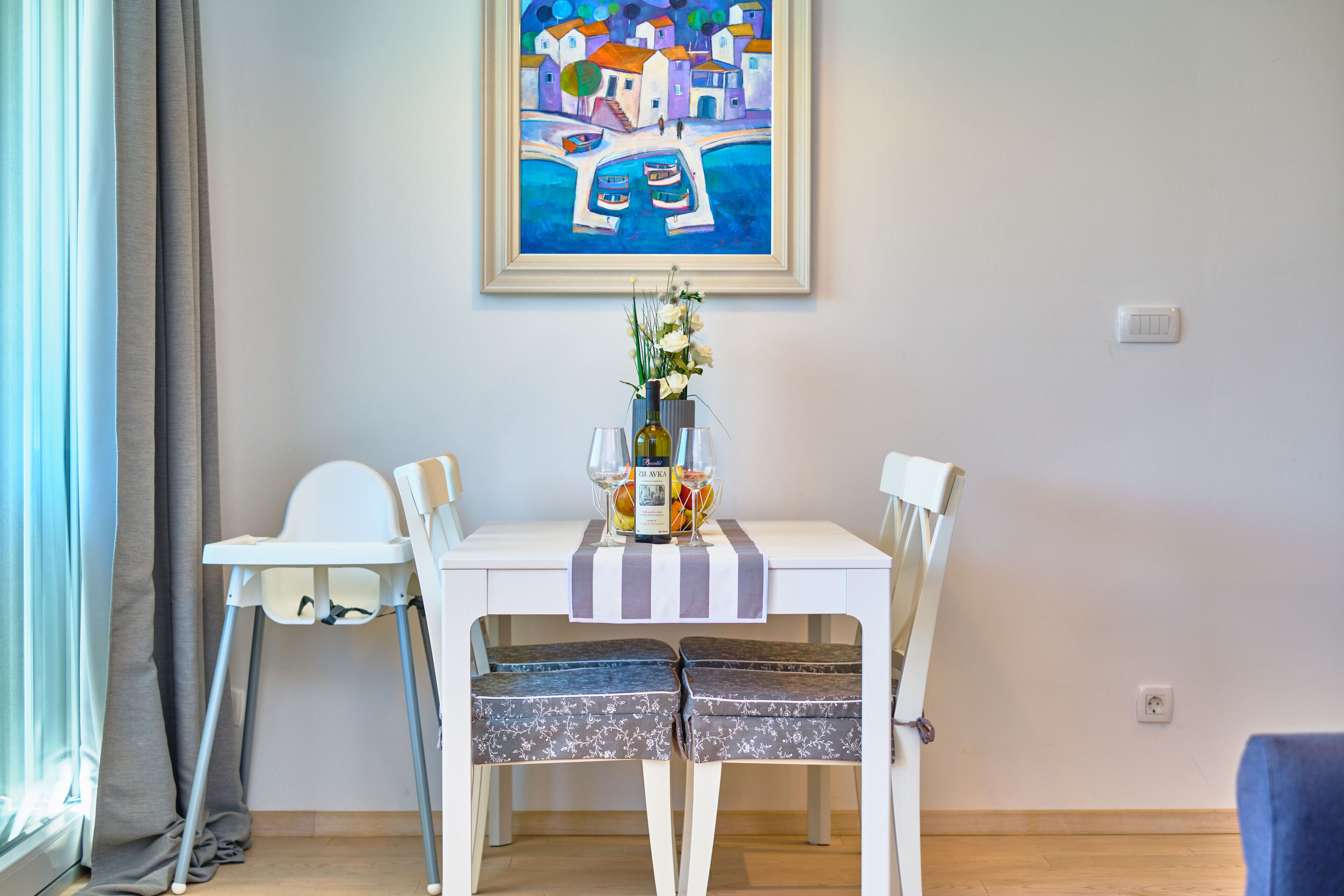 A dining area with a table, chairs, and a painting on the wall.