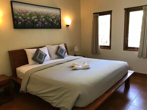 A neatly made bed with pillows, a bedside lamp, and a painting of flowers on the wall.
