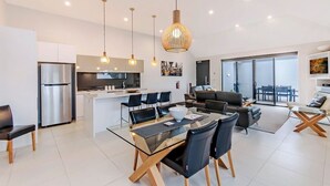 Une cuisine moderne dotée d’un réfrigérateur en acier inoxydable, un coin repas avec une table et des chaises en verre, et un salon avec un canapé et une table basse.