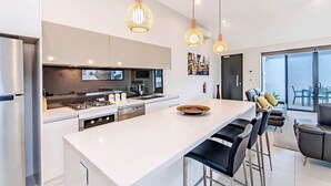 Une cuisine moderne dotée d’un îlot central, d’appareils électroménagers en acier inoxydable et de luminaires suspendus.