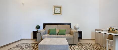 Una sala de estar con sofá, reposapiés y una mesita con objetos decorativos.