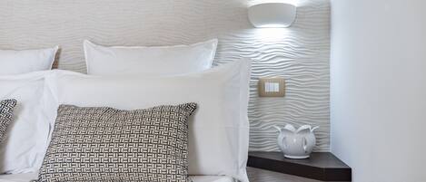 A neatly made bed with white and patterned pillows, a textured wall, and a bedside table with a white vase.