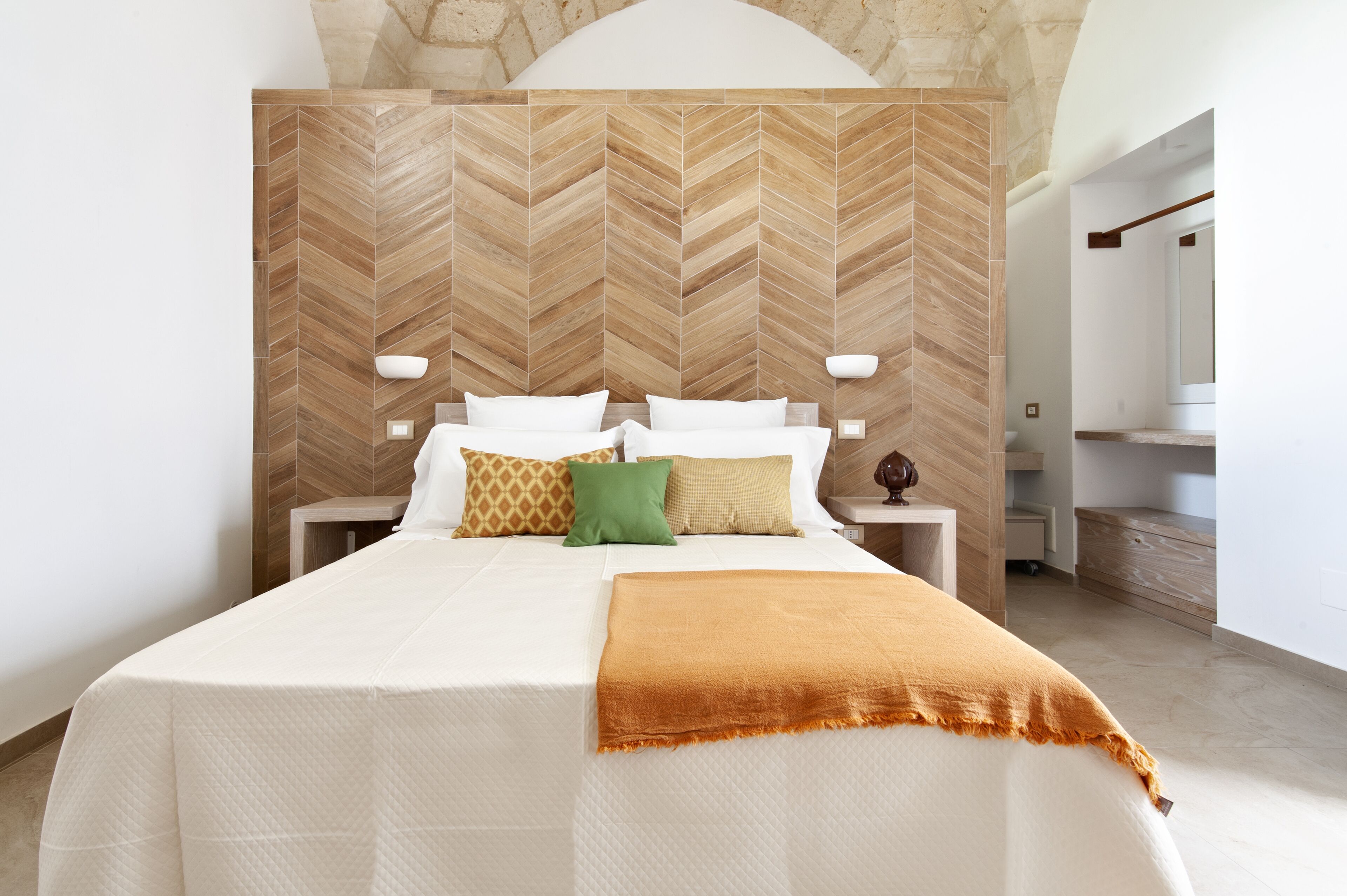 Un dormitorio moderno con cabecera estampada en patrón de espiga, una cama grande con ropa blanca y una manta marrón.