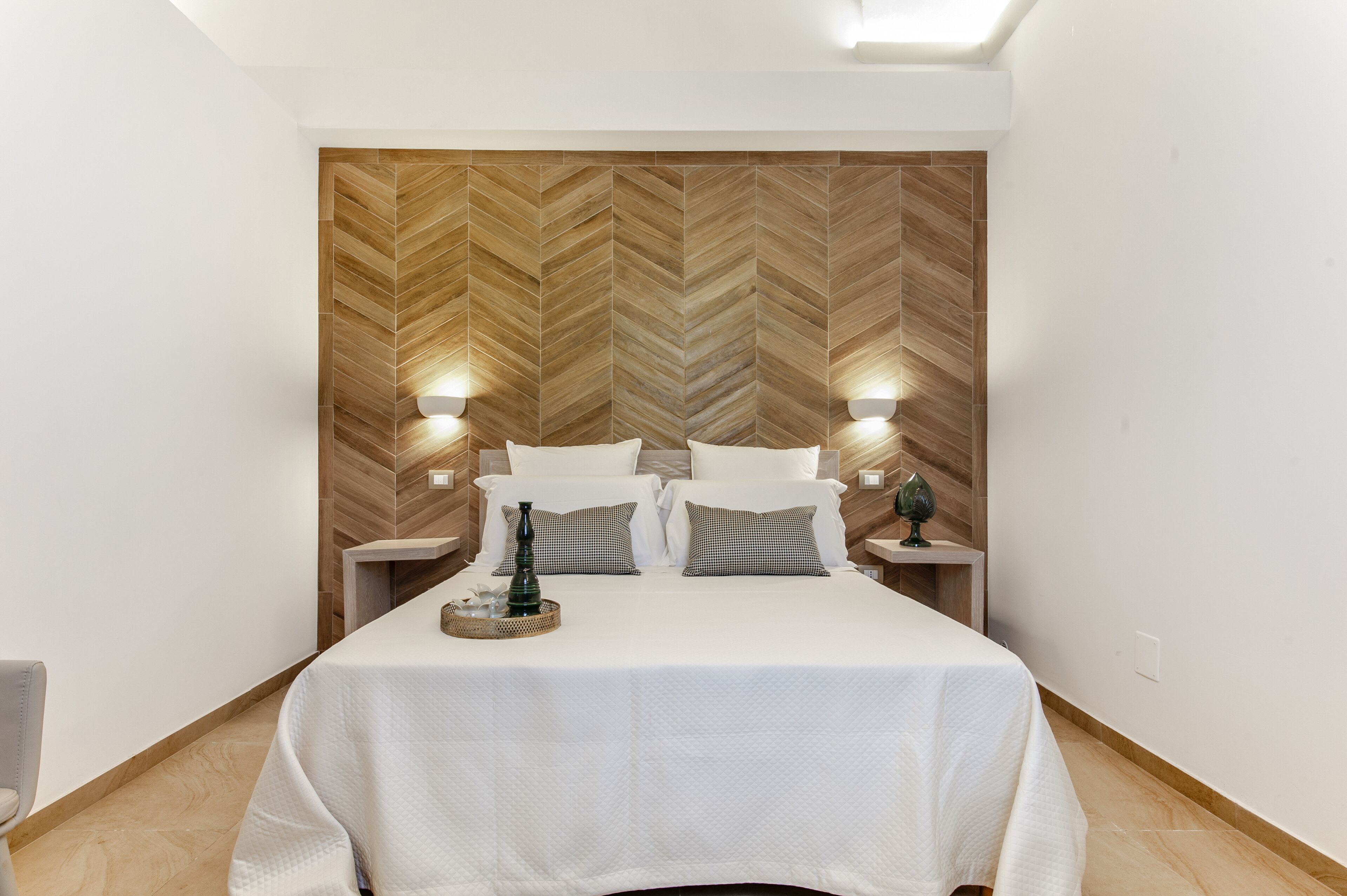 A neatly made bed with white linens, two bedside tables with lamps, and a herringbone-patterned wooden headboard.