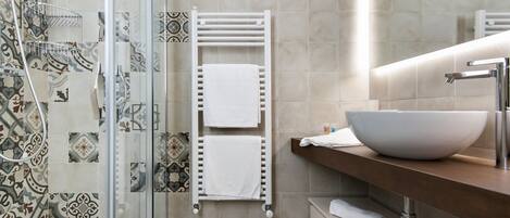 A modern bathroom with a glass shower enclosure, a white towel rack, a large white vessel sink, and patterned tiles on the walls.