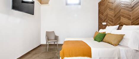 A bedroom with a bed, a chair, a TV mounted on the wall, and a window.