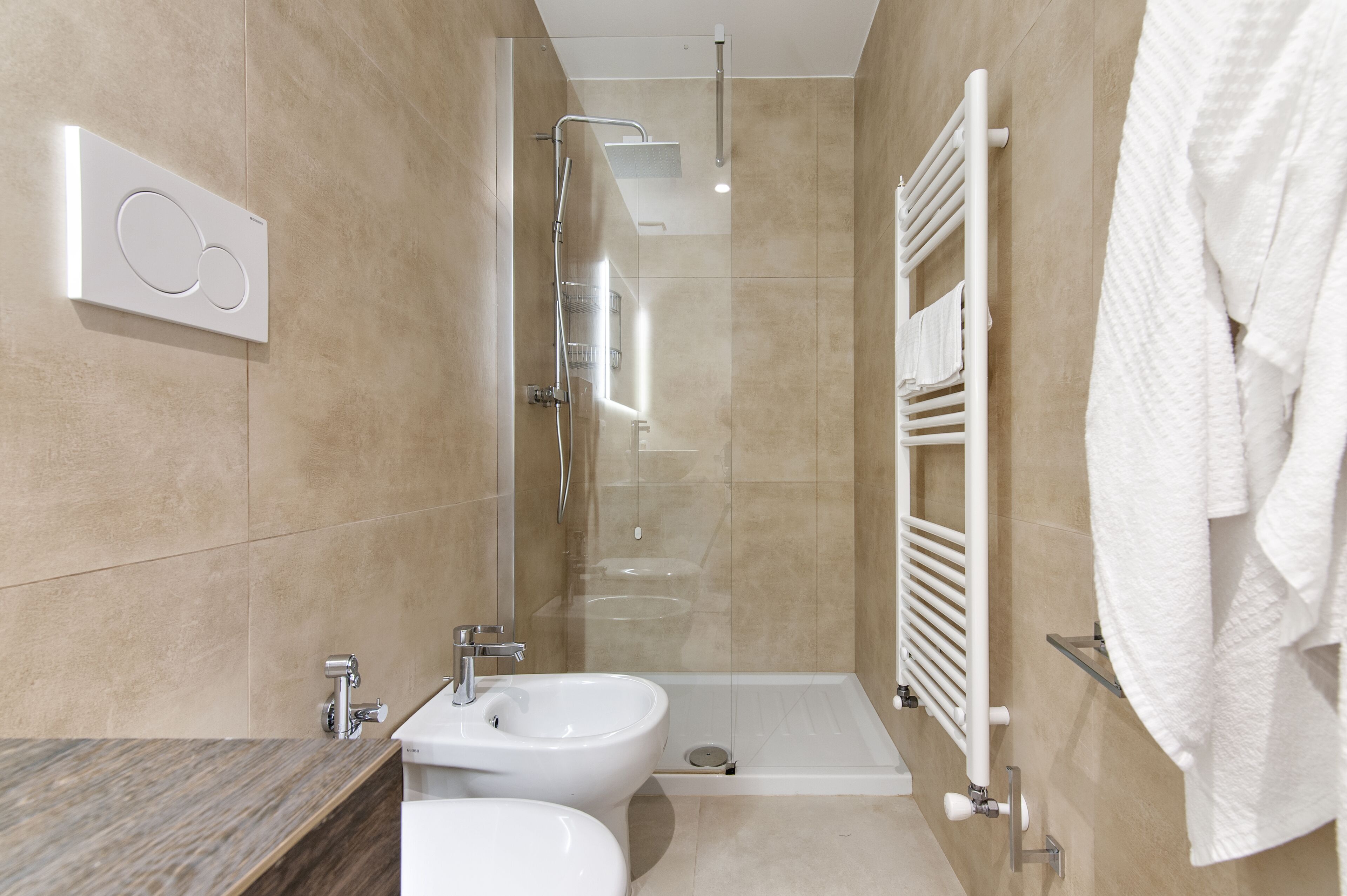 Un baño moderno con ducha de vidrio, un bidé y un perchero para toallas.
