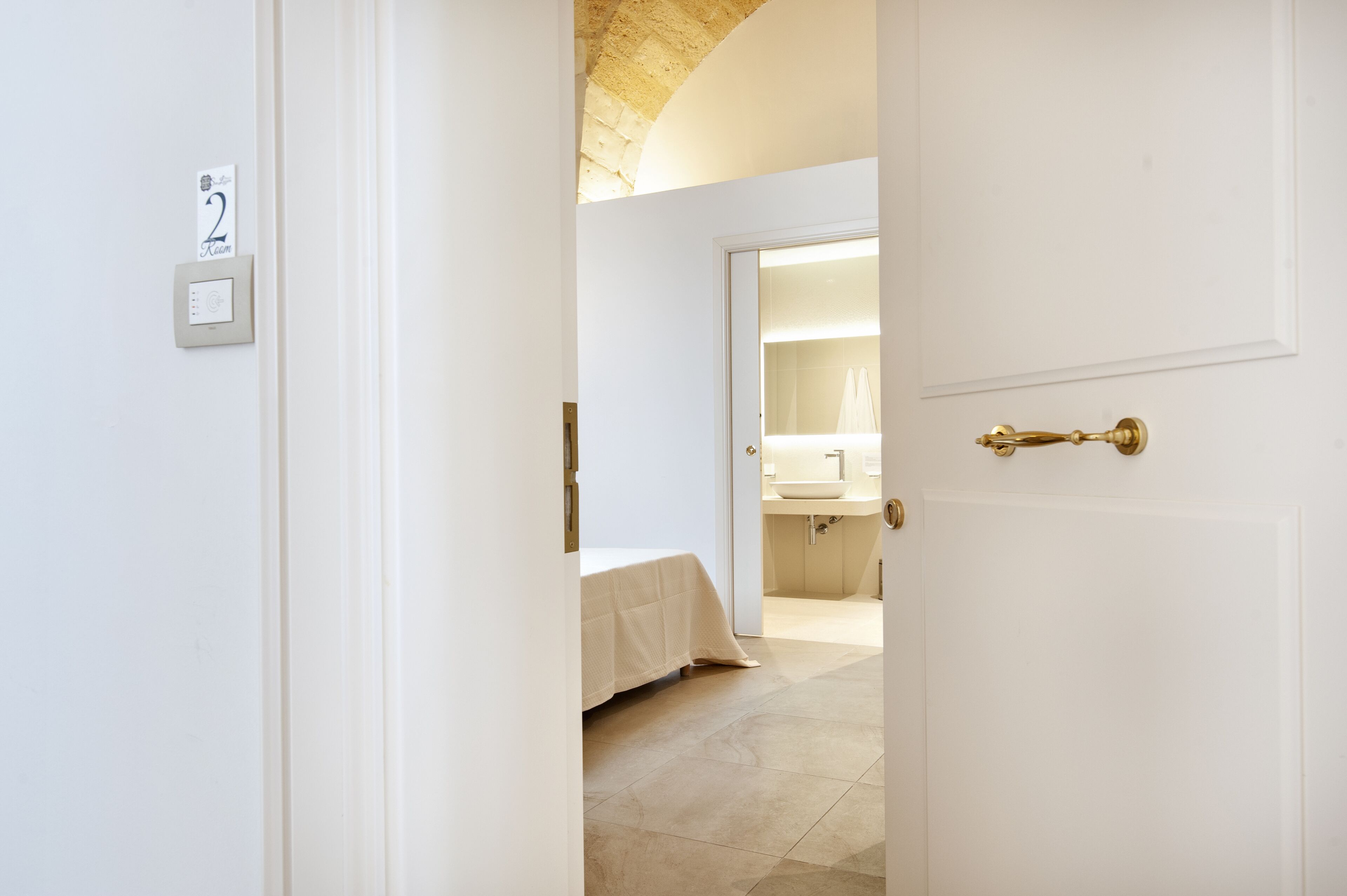 A hotel room with a bed, a bathroom with a sink, and a door with a brass handle.
