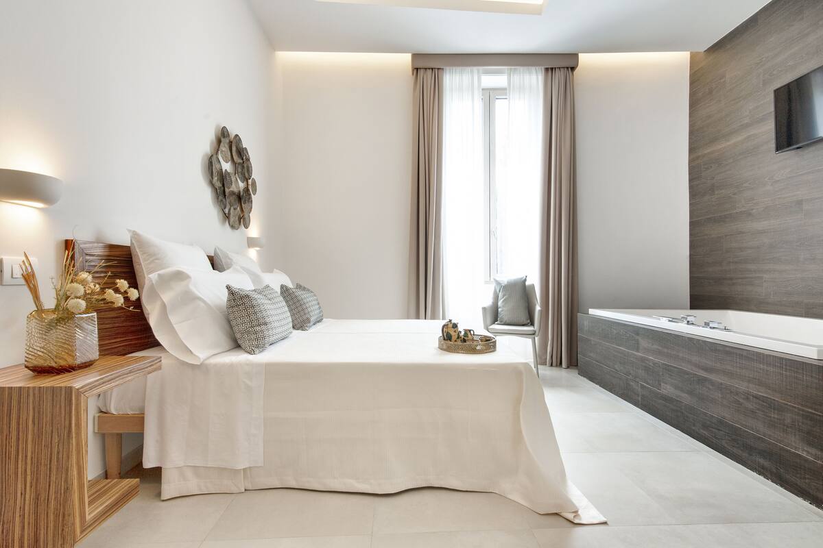 Ein modernes Schlafzimmer mit einem großen Bett, einem Nachttisch mit einer Vase und Blick auf ein Badezimmer mit einer Badewanne.