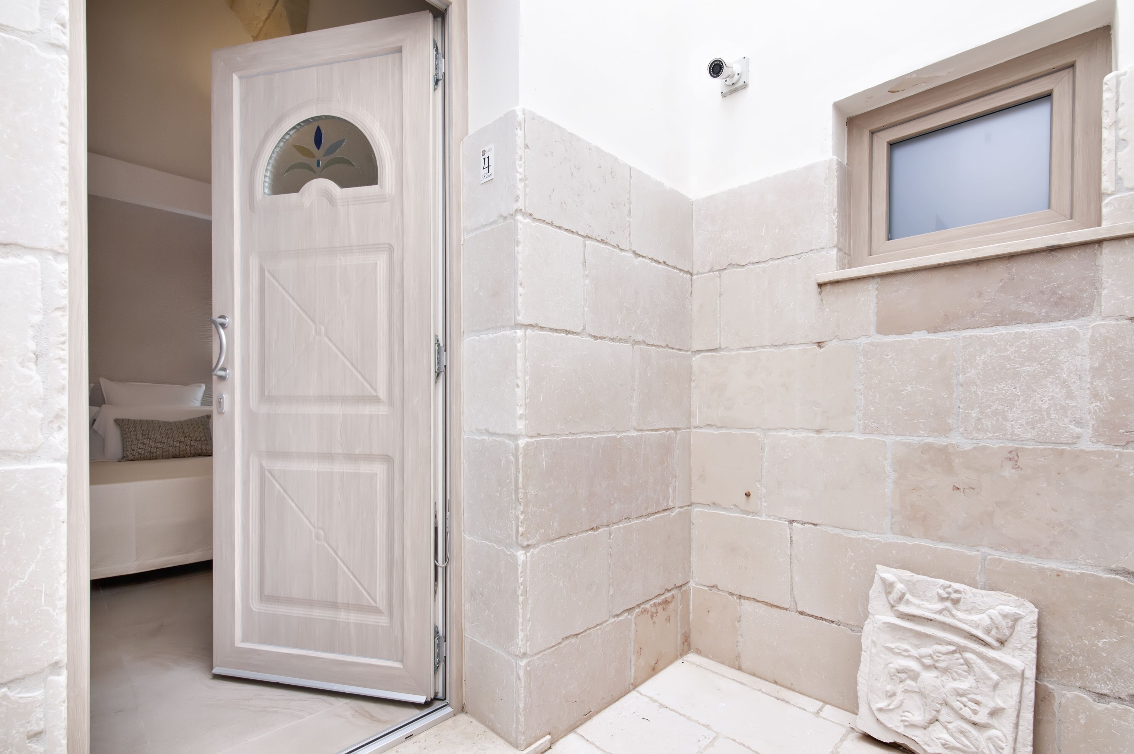 Une pièce avec une porte blanche, une petite fenêtre et un mur en pierre.