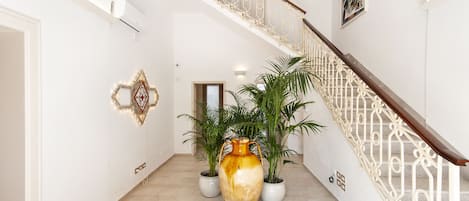 A hallway with a large vase, potted plants, and a staircase with a white railing.