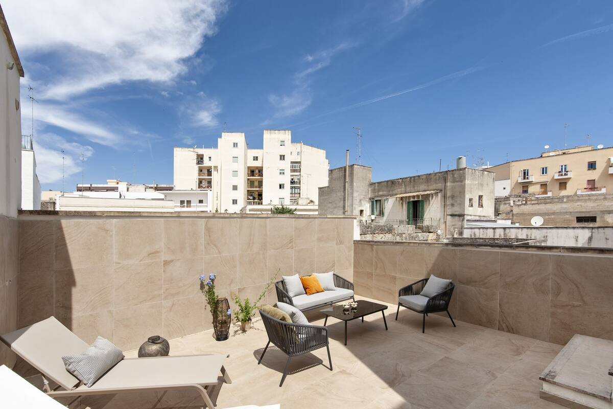 Eine Dachterrasse mit beigefarbenen Fliesen, einer Sofagruppe, einem Couchtisch und einem Lounge-Sessel.