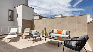 Terraza en la azotea con un sofá, dos sillones, una mesita de centro y una pequeña planta en maceta.