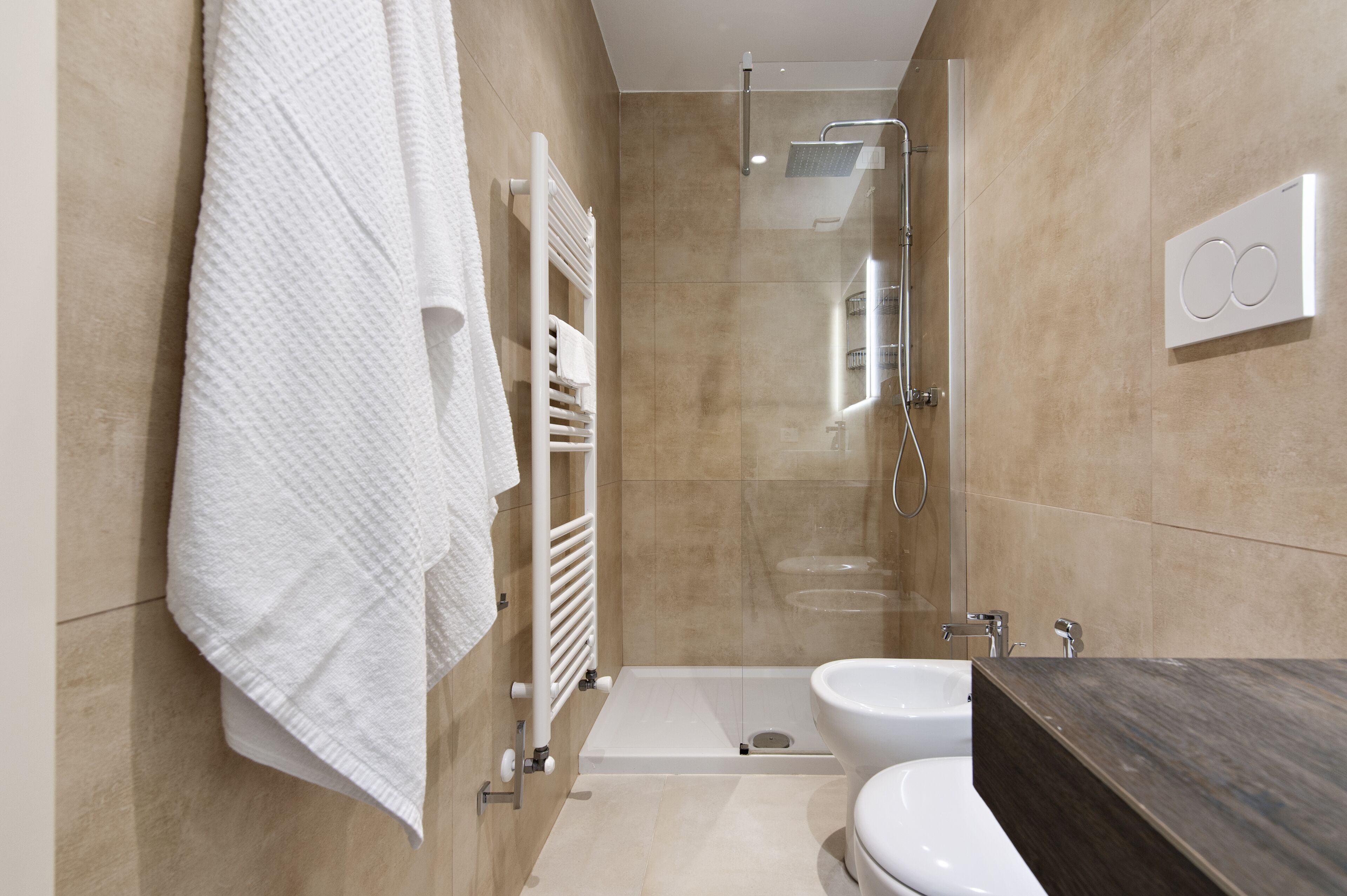 A modern bathroom with a glass-enclosed shower, a white bathtub, and a dark wooden vanity.