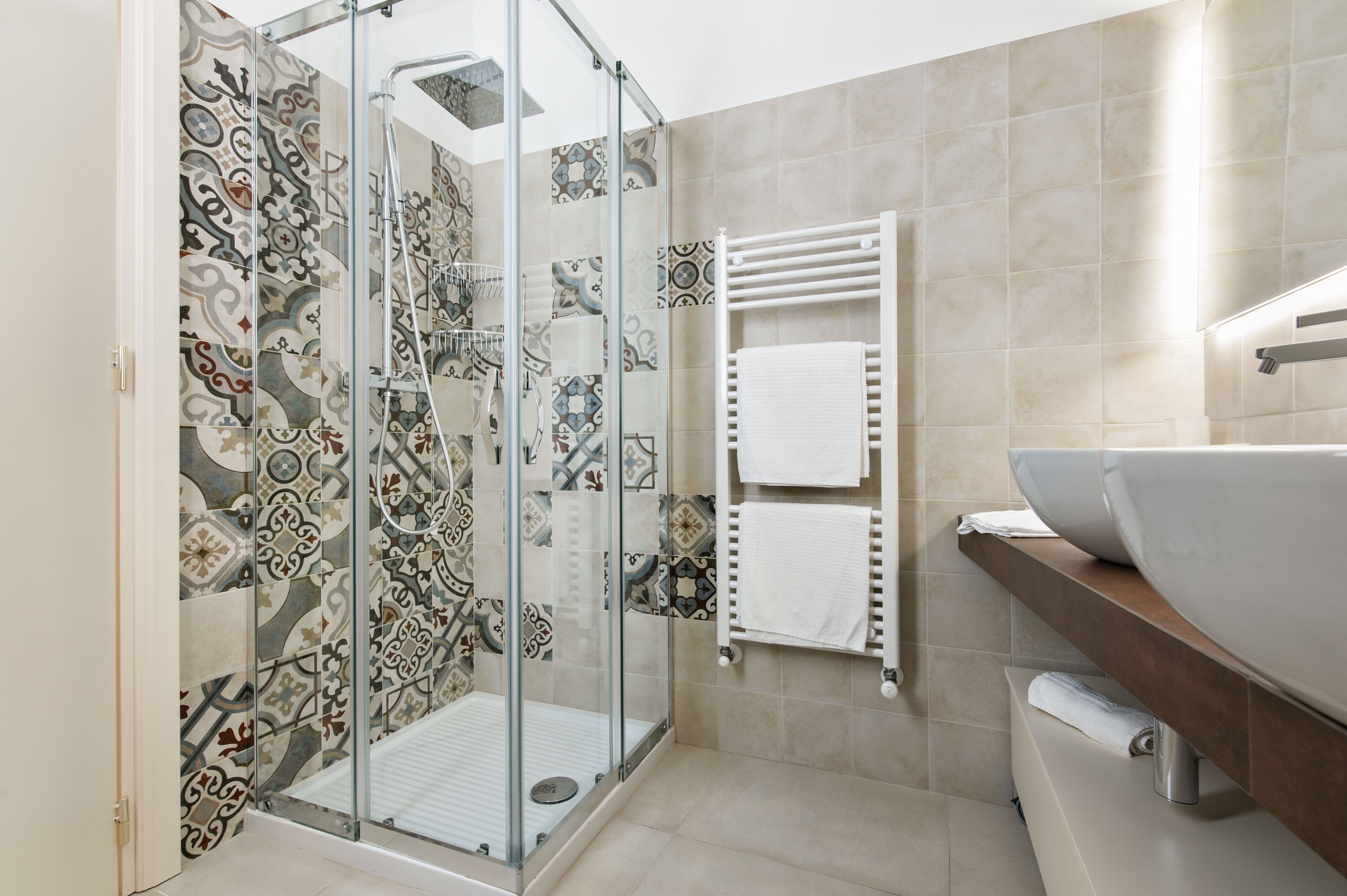Une salle de bain moderne avec une douche à parois de verre, des carreaux à motifs, un lavabo blanc et un porte-serviettes.