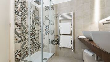 Une salle de bain moderne avec une douche à parois de verre, des carreaux à motifs, un lavabo blanc et un porte-serviettes.