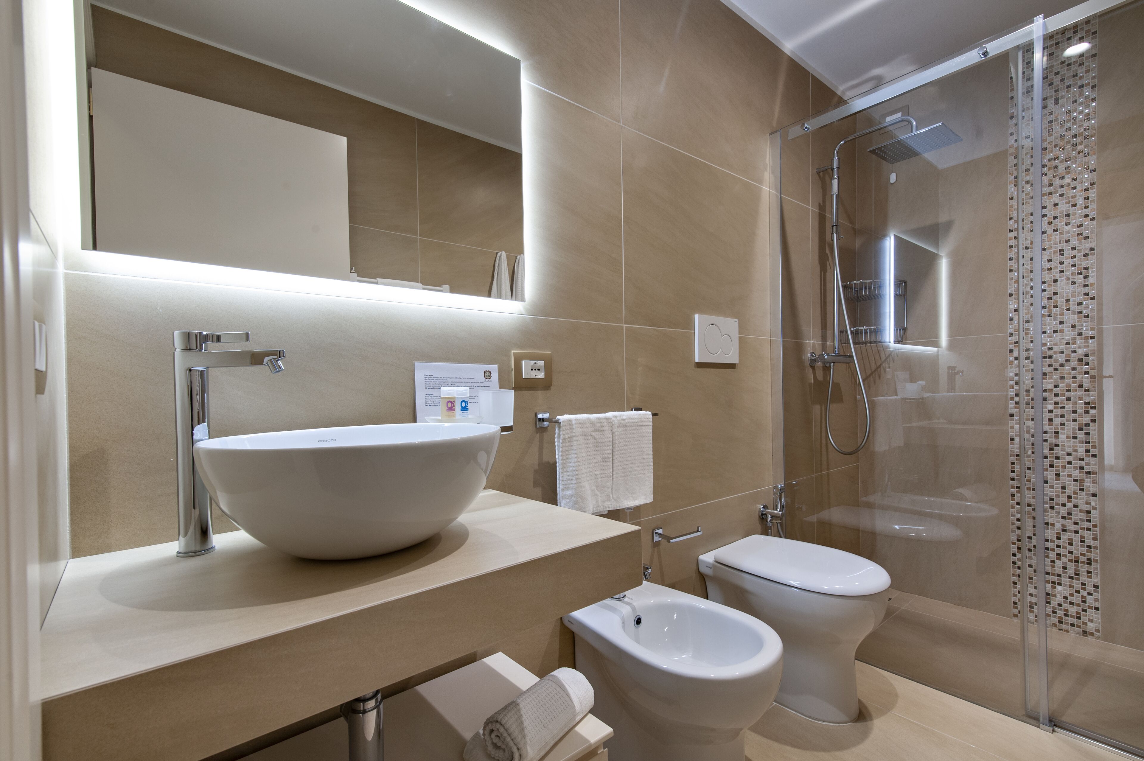 A modern bathroom with a large vessel sink, a toilet, a bidet, and a glass-enclosed shower.