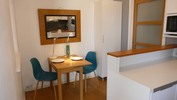 A compact dining area with a wooden table, two blue chairs, a white lamp, and a mirror above the table. - T1 Parking Inclus, Hyper Centre, Mais Très Calme (Pau)