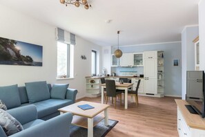 En moderne stue med sofa, spisebord og et køkken med hvide skabe og en træbordplade.